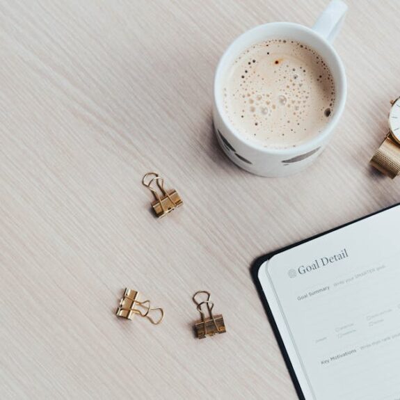 A minimalist desk arrangement featuring a coffee cup, notebook, pen, and wristwatch.
