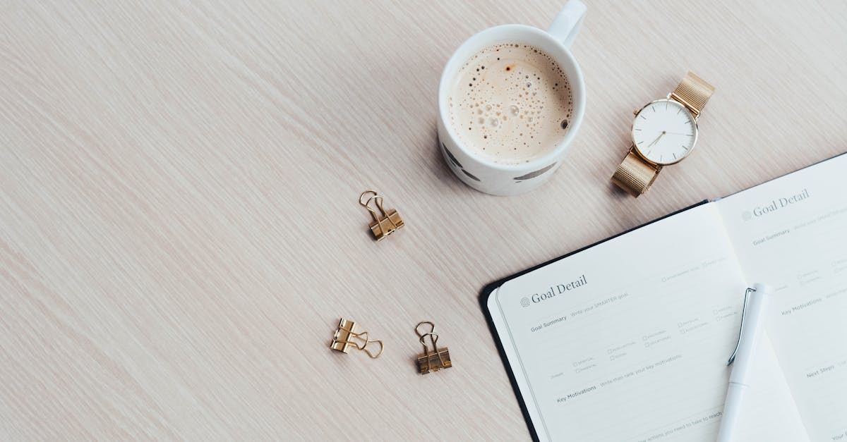 A minimalist desk arrangement featuring a coffee cup, notebook, pen, and wristwatch.