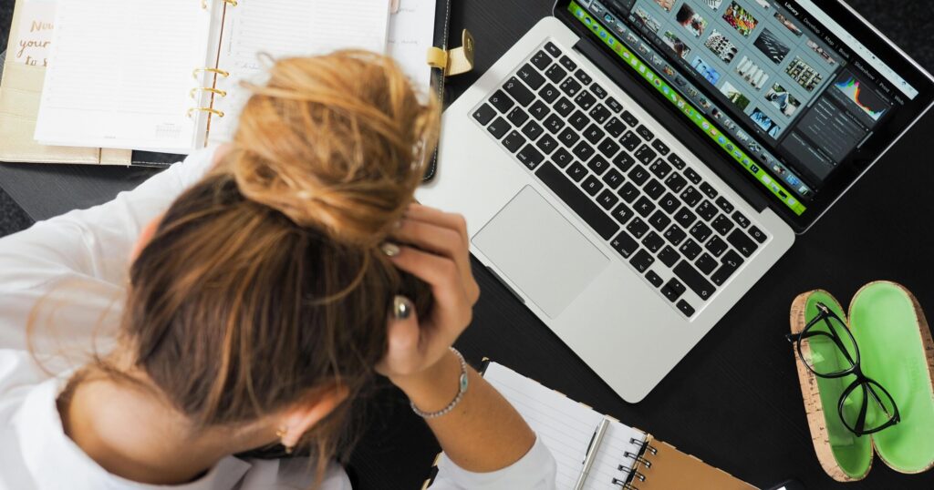 Overhead view of a stressed woman working at a desk with a laptop, phone, and notebooks.