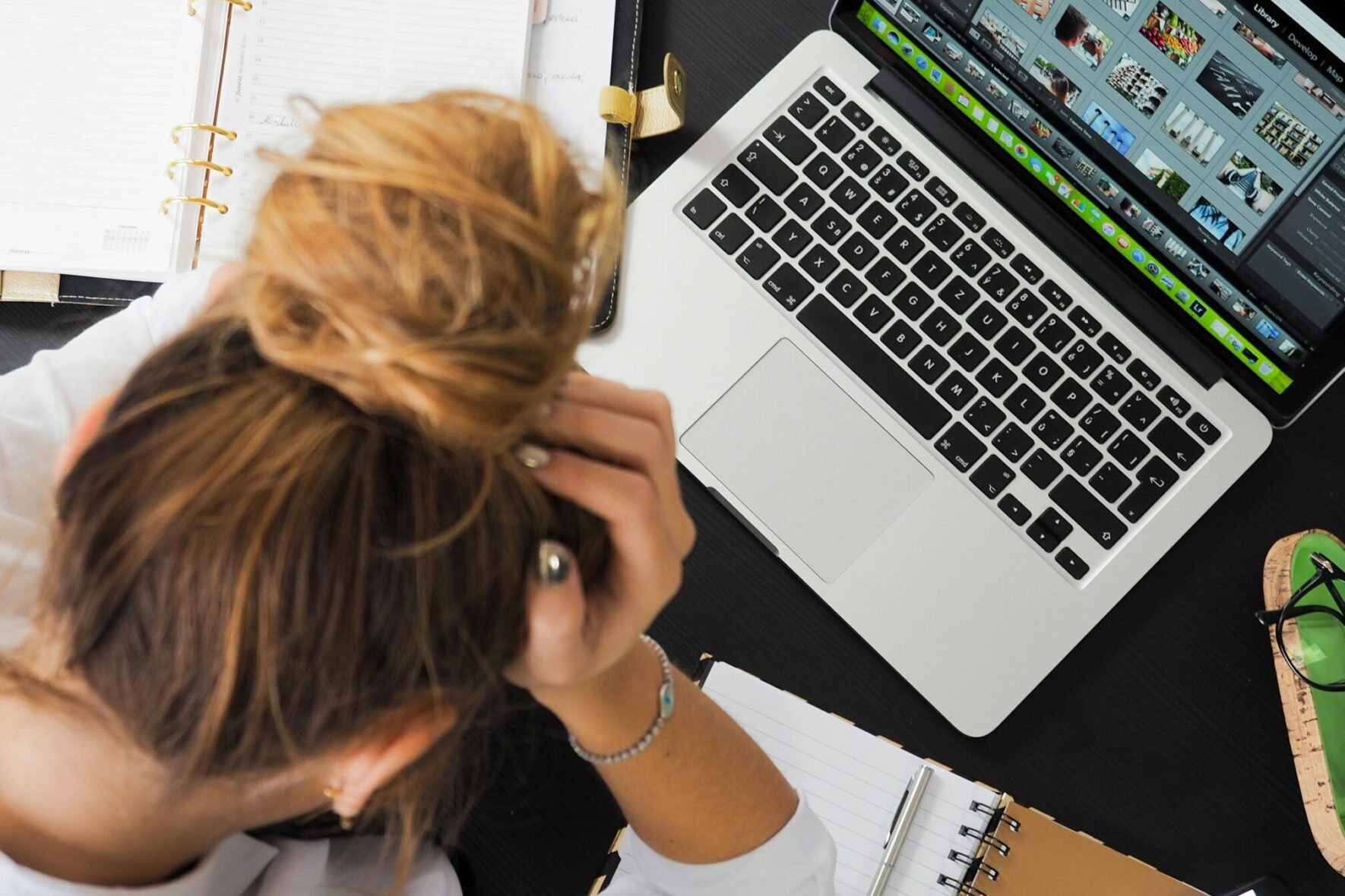 Overhead view of a stressed woman working at a desk with a laptop, phone, and notebooks.